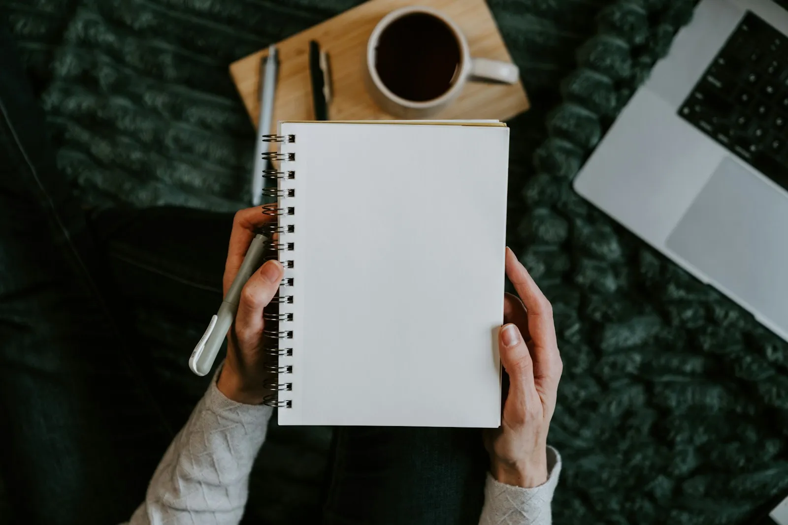 Iemand die schrijft in een notitieboek bij een kop koffie op een houten tafel